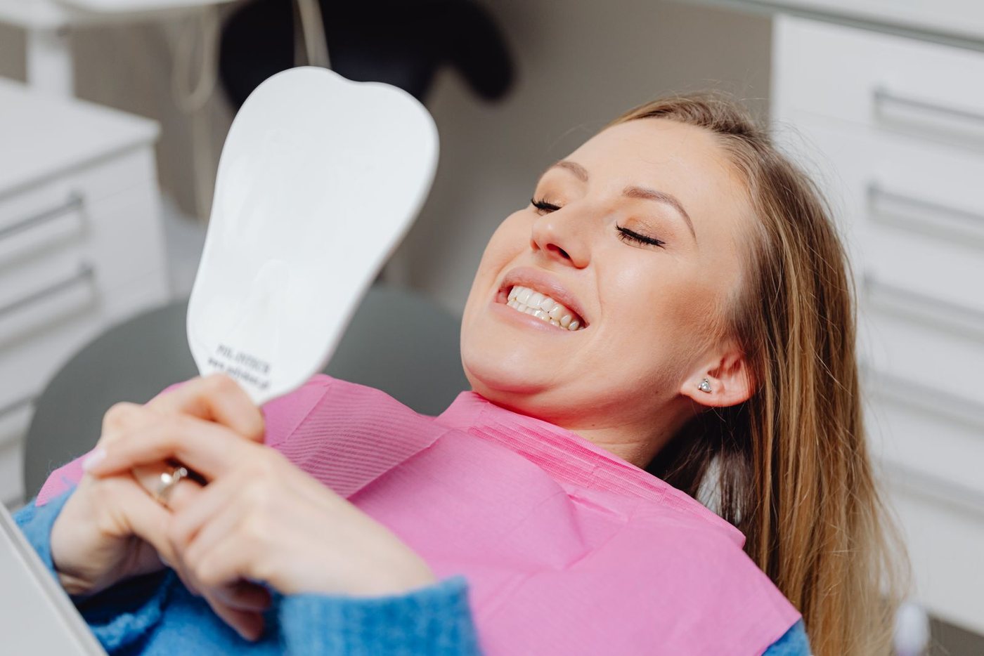 Woman smiling at her straightened teeth in a hand mirror after clear aligner treatment